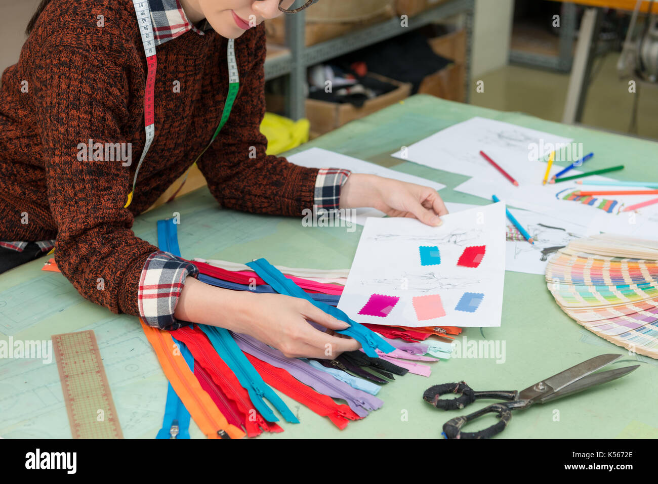 Giovani belle produttore di abbigliamento femminile azienda dipendente utilizzando designer file di disegno carta scegliendo colore giusto zipper. Foto Stock