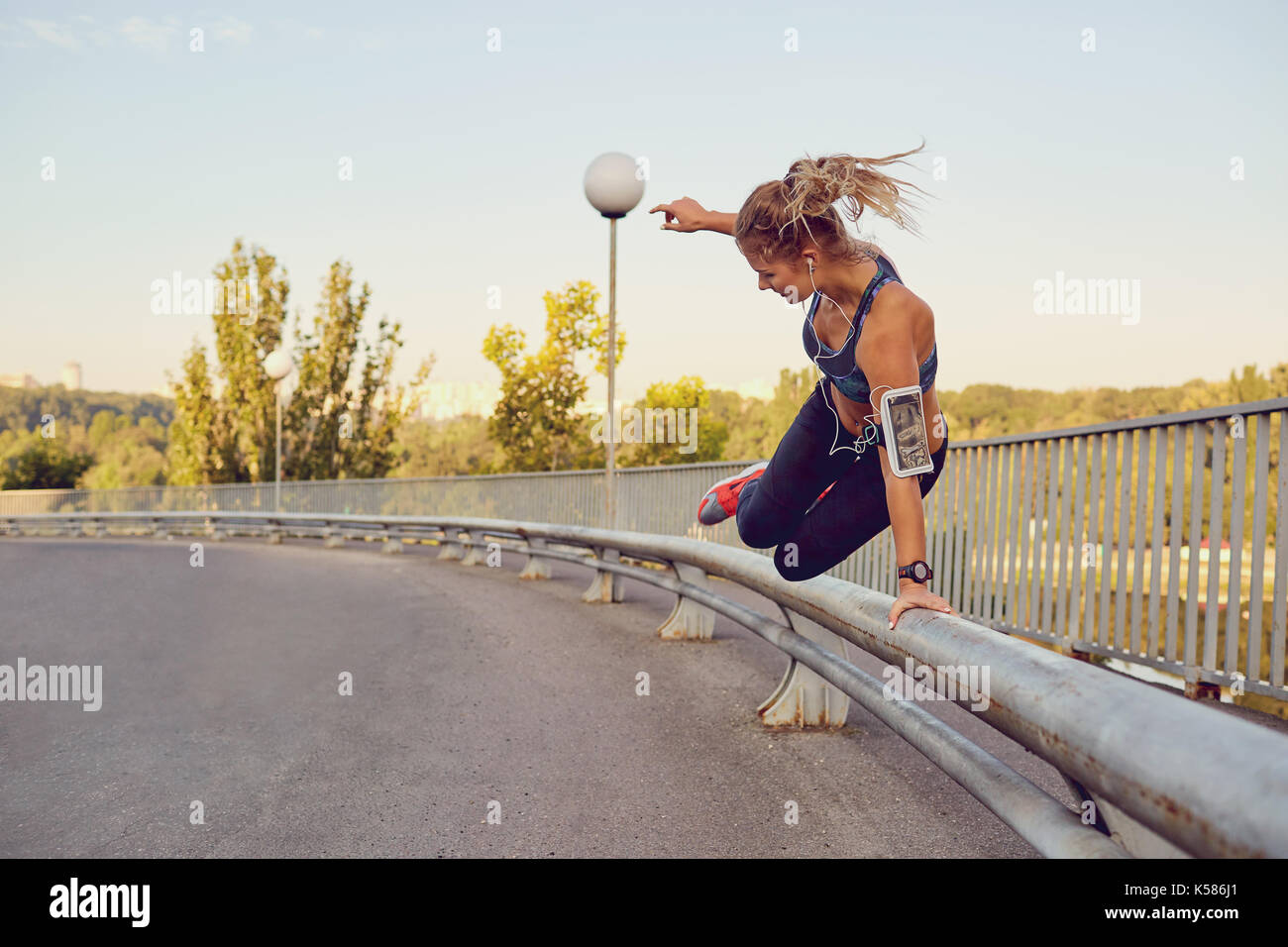 Una ragazza runner salta sopra una ringhiera su un ponte della città. Foto Stock
