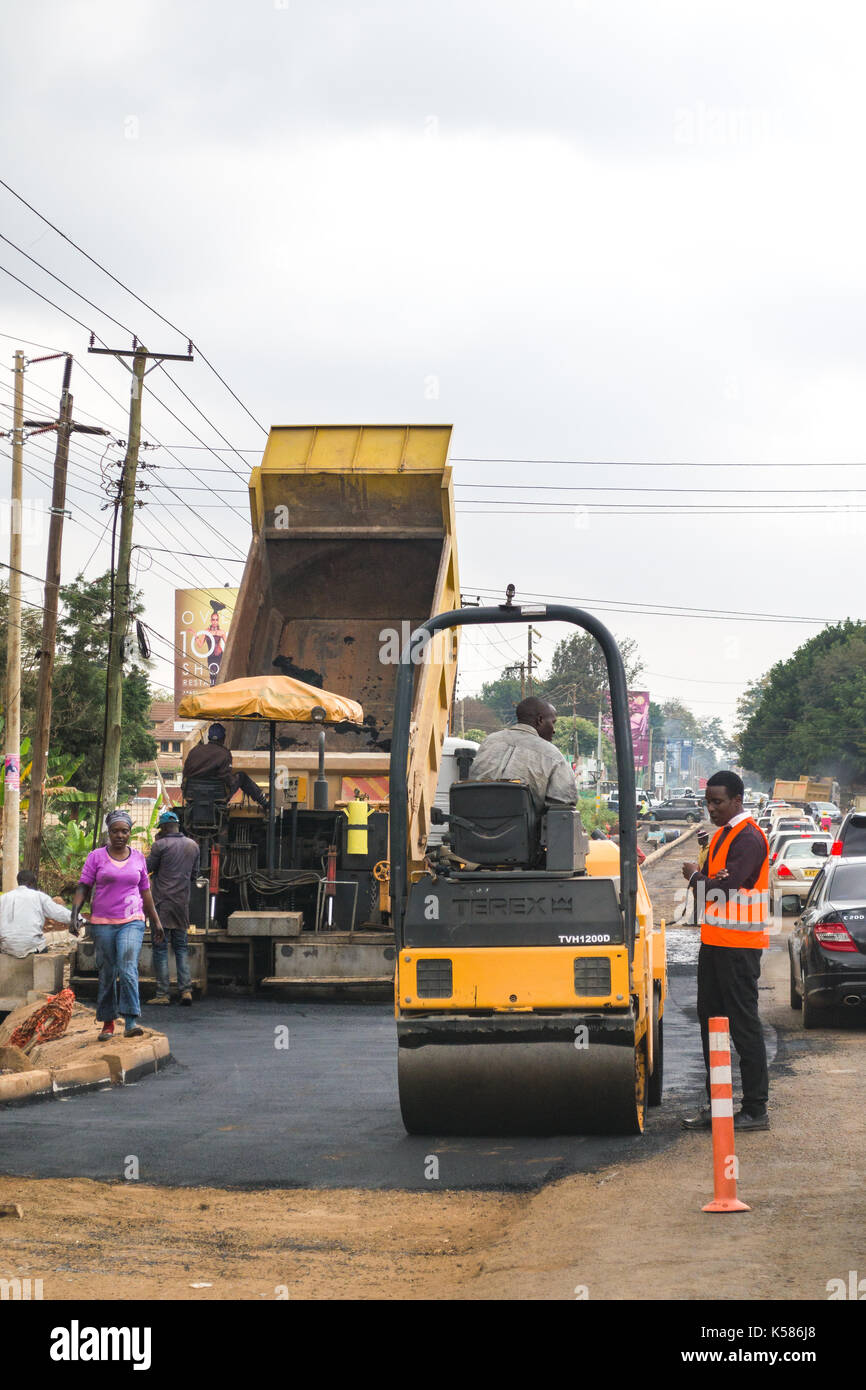 I veicoli della costruzione della strada asfaltata versatore mentre le unità di traffico passato, Nairobi, Kenia Foto Stock