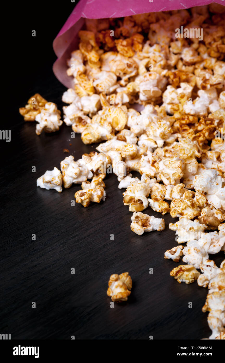 Popcorn sparsi sul legno scuro dello sfondo con paio di occhiali 3d. luminose movie argomento. fast food. rosa scatola di carta. la visione di cinema. Foto Stock