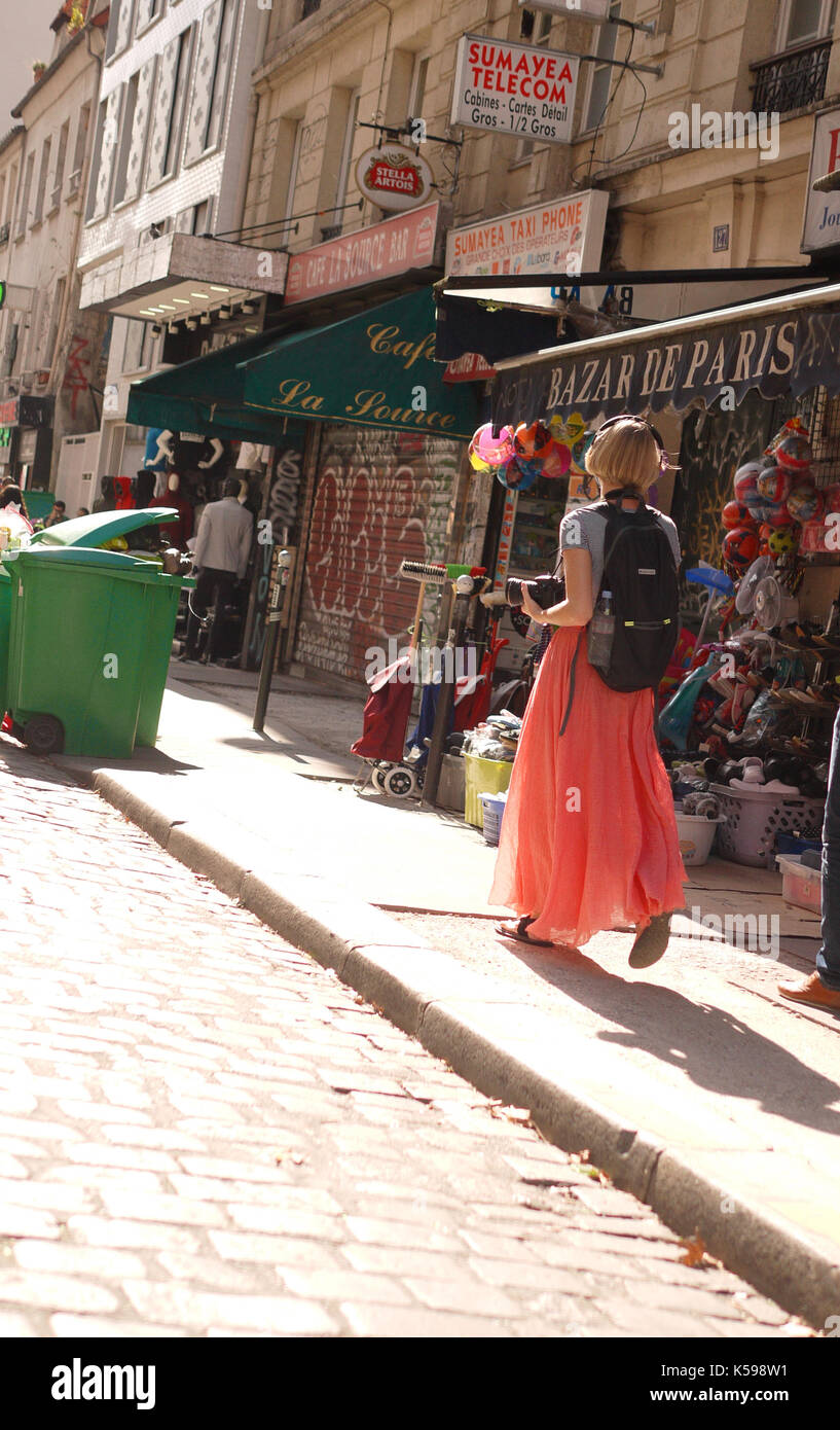 Una ragazza in un abito arancione esplora le strade di Parigi con la sua macchina fotografica. Foto Stock