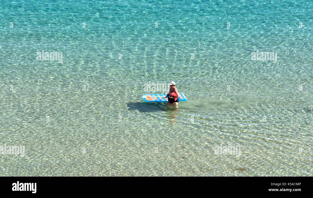 Una donna spingendo un blu e giallo Lilo attraverso il mare poco profondo e acqua Menorca Minorca Foto Stock