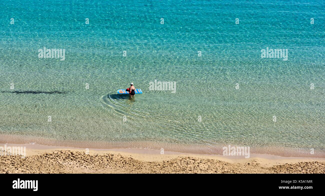 Una donna spingendo un blu e giallo Lilo attraverso il mare poco profondo e acqua Menorca Minorca Foto Stock