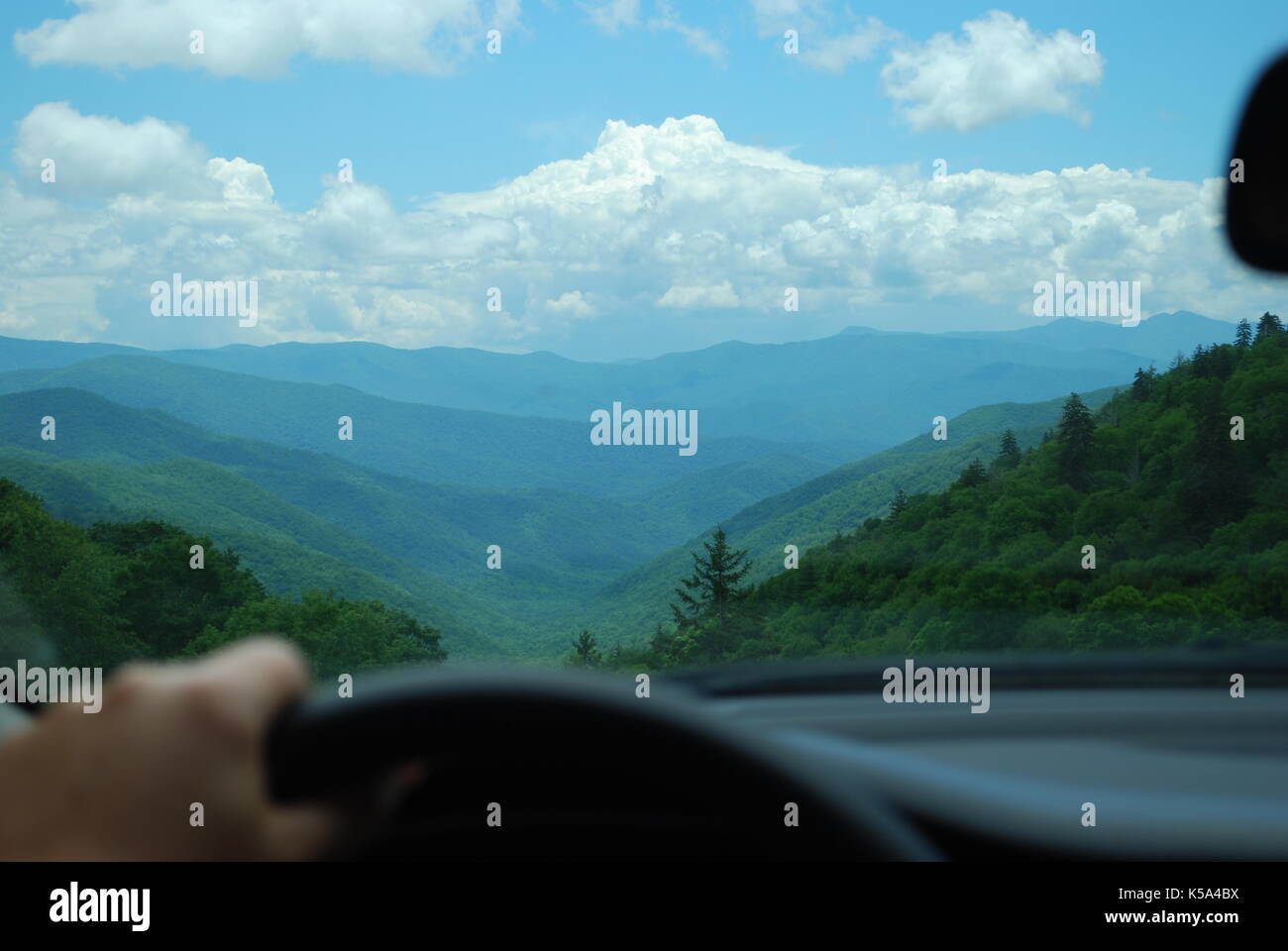 Maschio di mano sul volante. Ampia vista attraverso l'auto anteriore finestra sul paesaggio delle montagne Foto Stock