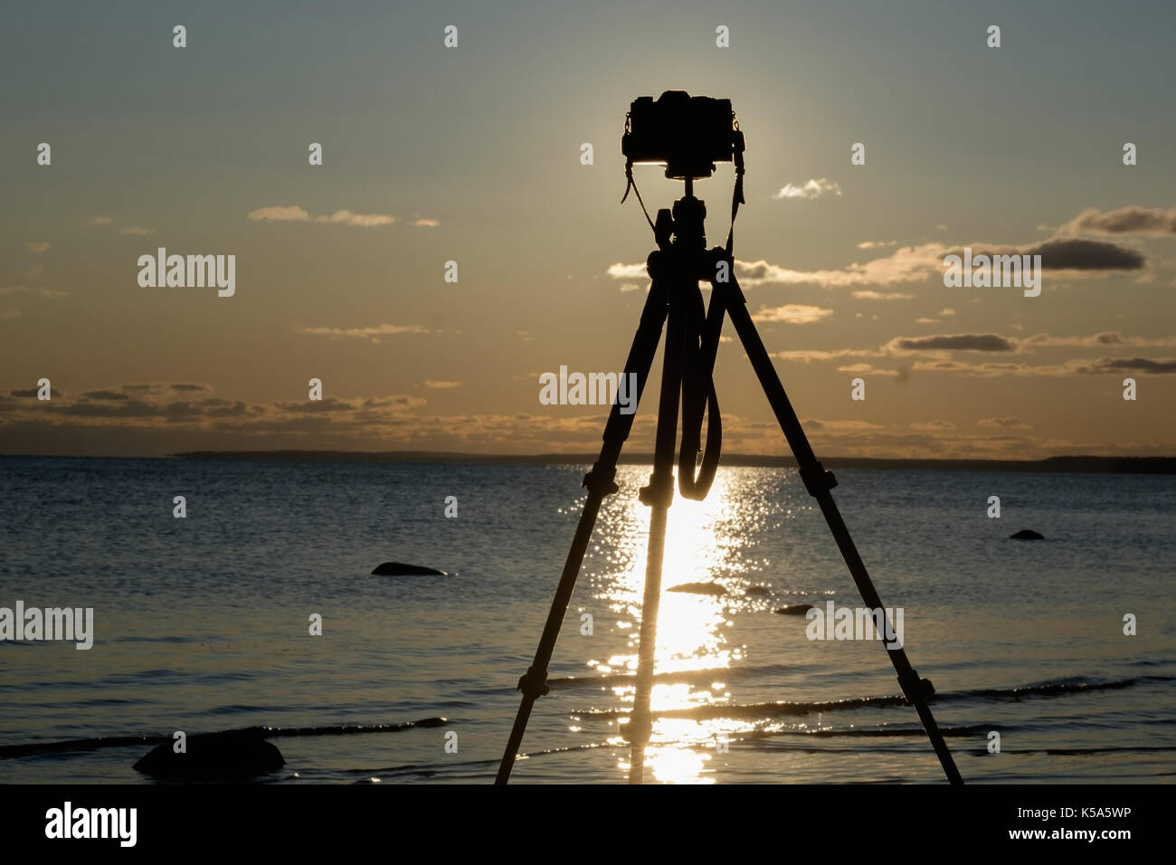 Fotocamera con treppiede oltre il tramonto vicino acqua di mare Foto Stock