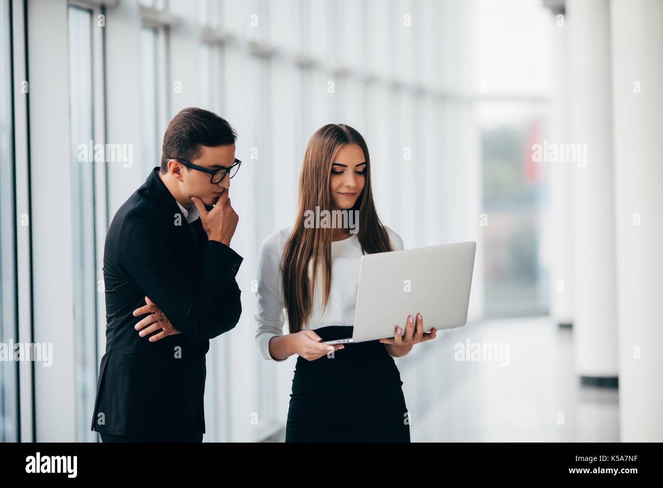 Moderna azienda giovane gente che lavora sul computer portatile in ufficio hall con finestre panoramiche discutere le future modifiche sul computer portatile Foto Stock