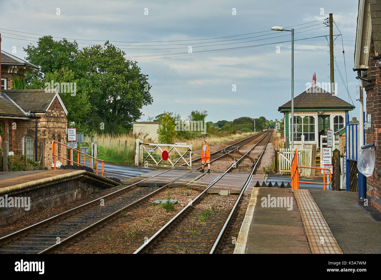 Segnalatore vestito in arancione alta visibilità tute manualmente il livello operativo attraversando i cancelli in corrispondenza delle zone rurali Lincolnshire stazione di Swinderby Foto Stock