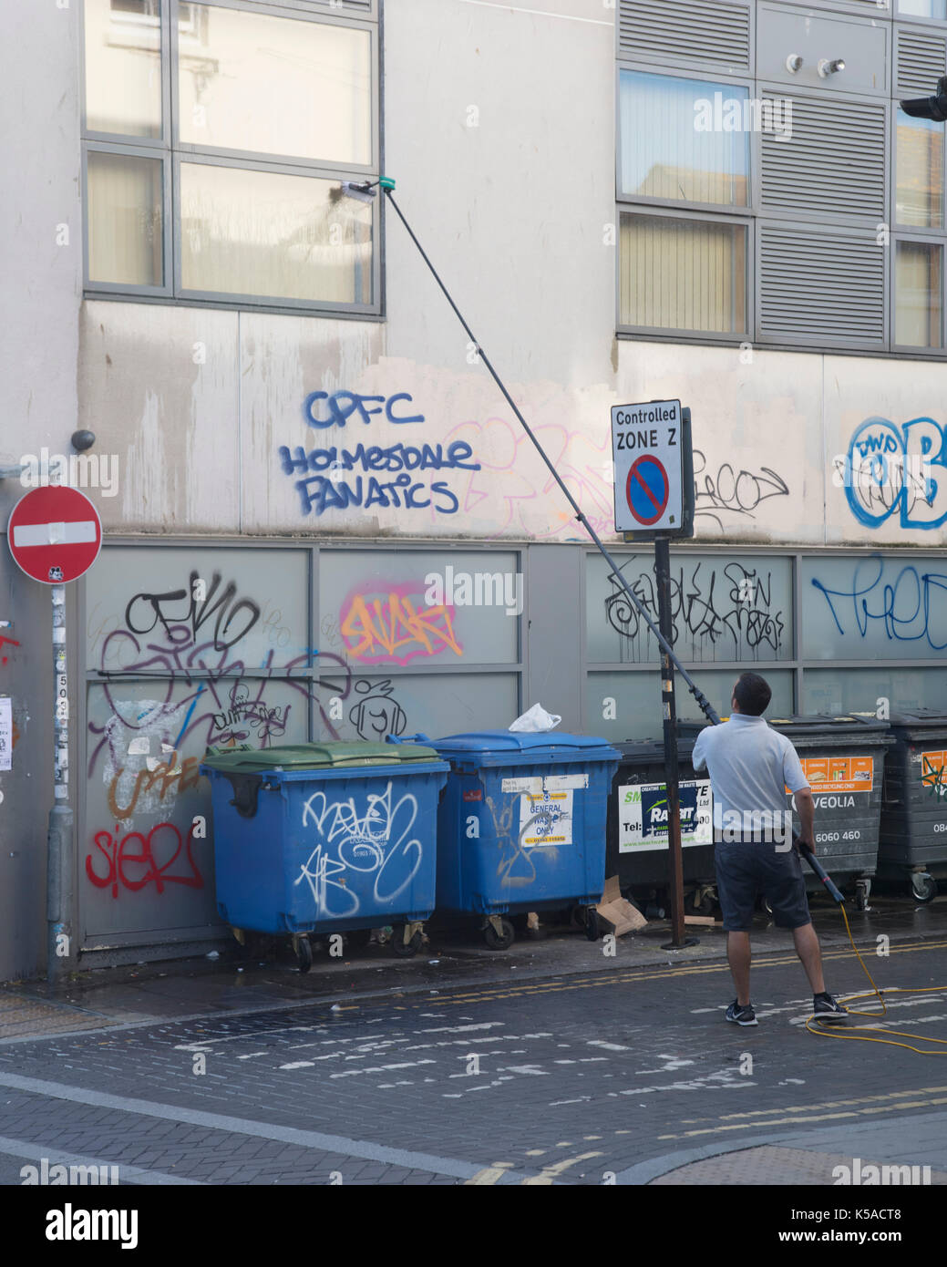 Detergente per vetri Pulizia alte finestre con manico lungo pennello in una strada urbana Foto Stock