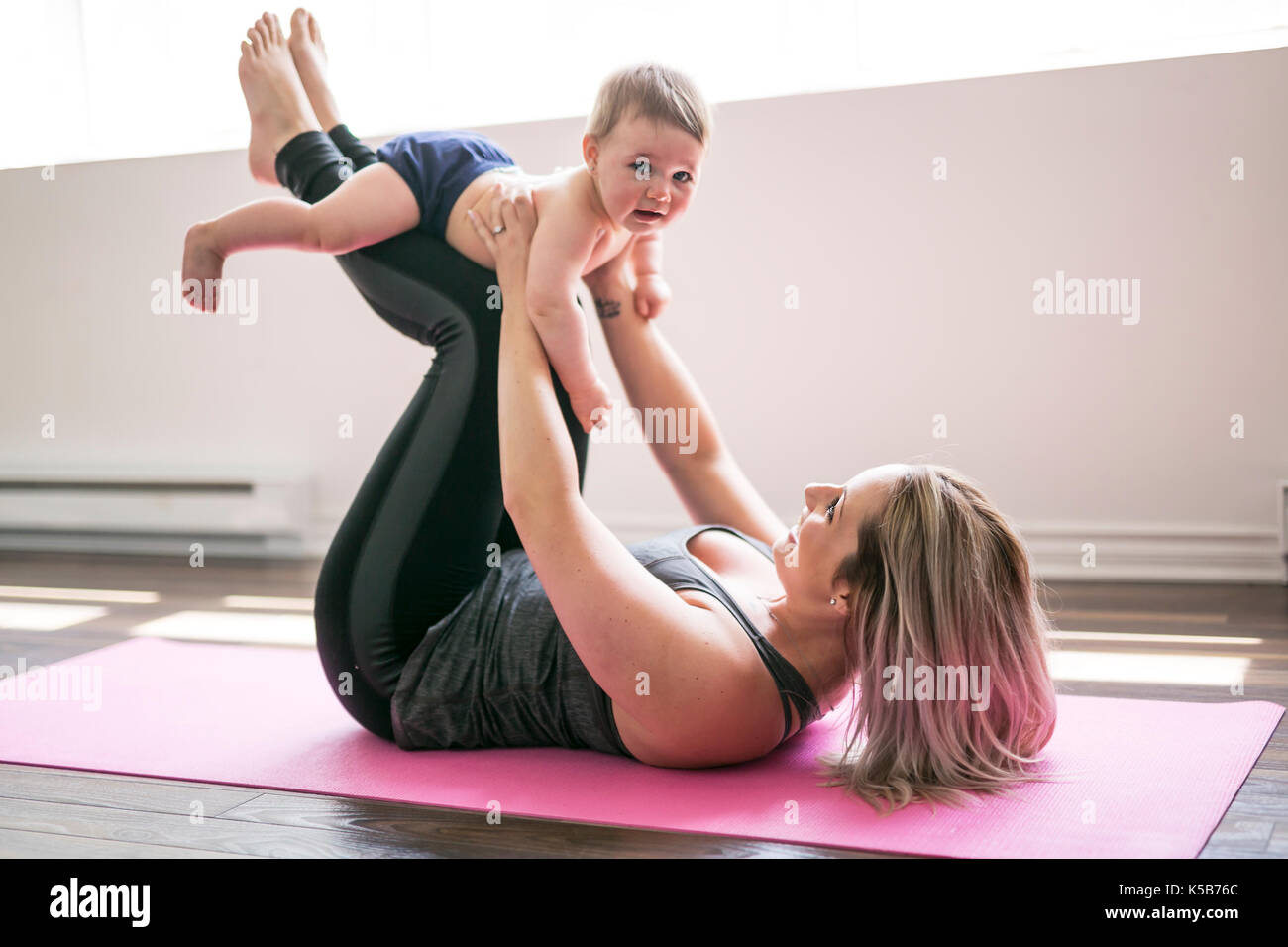 Giovane madre non fisico esercizi di yoga insieme con il suo bambino Foto Stock