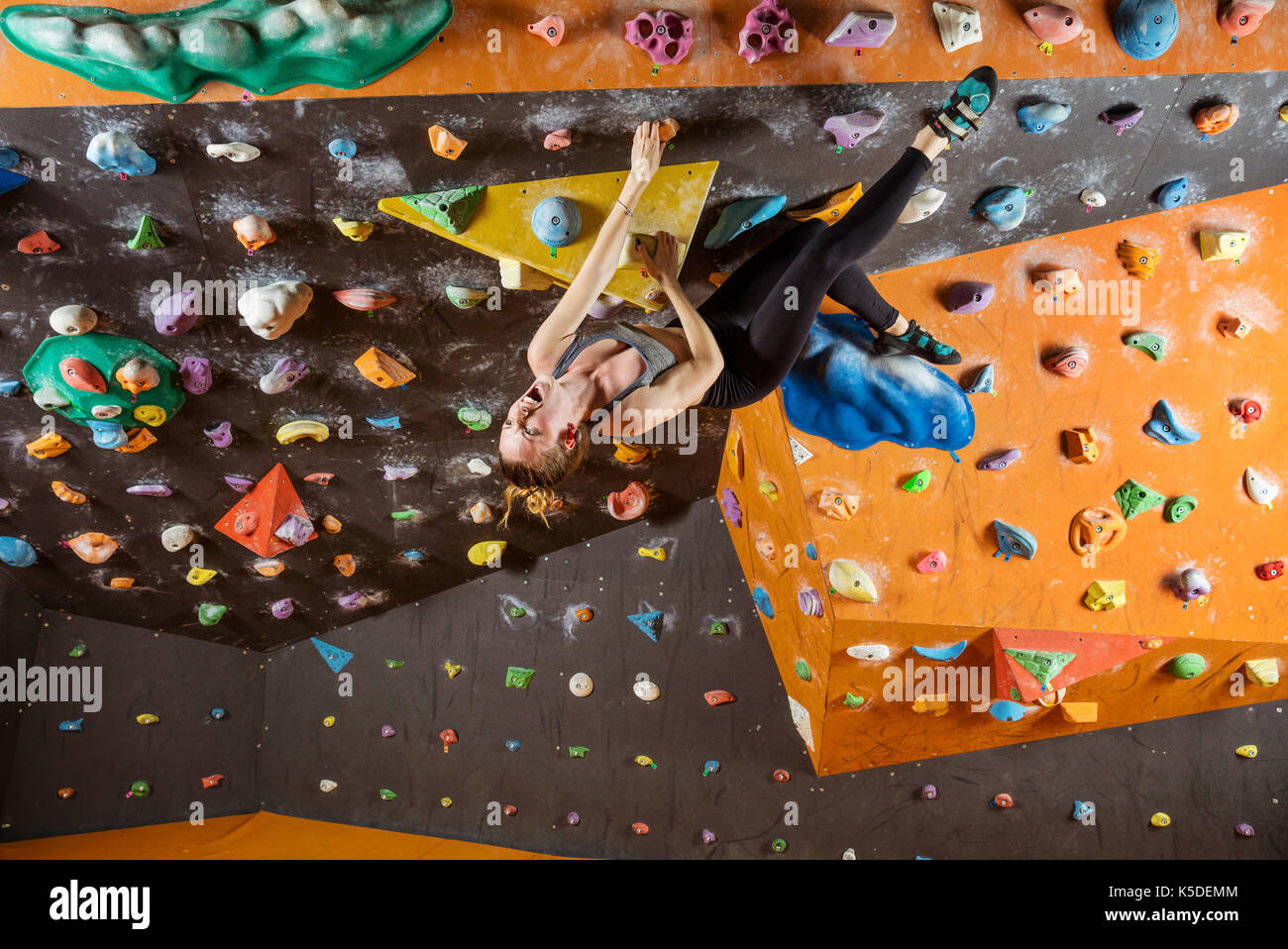 Espressivo giovane donna bouldering in palestra di arrampicata, lottando per risolvere problema stimolante Foto Stock