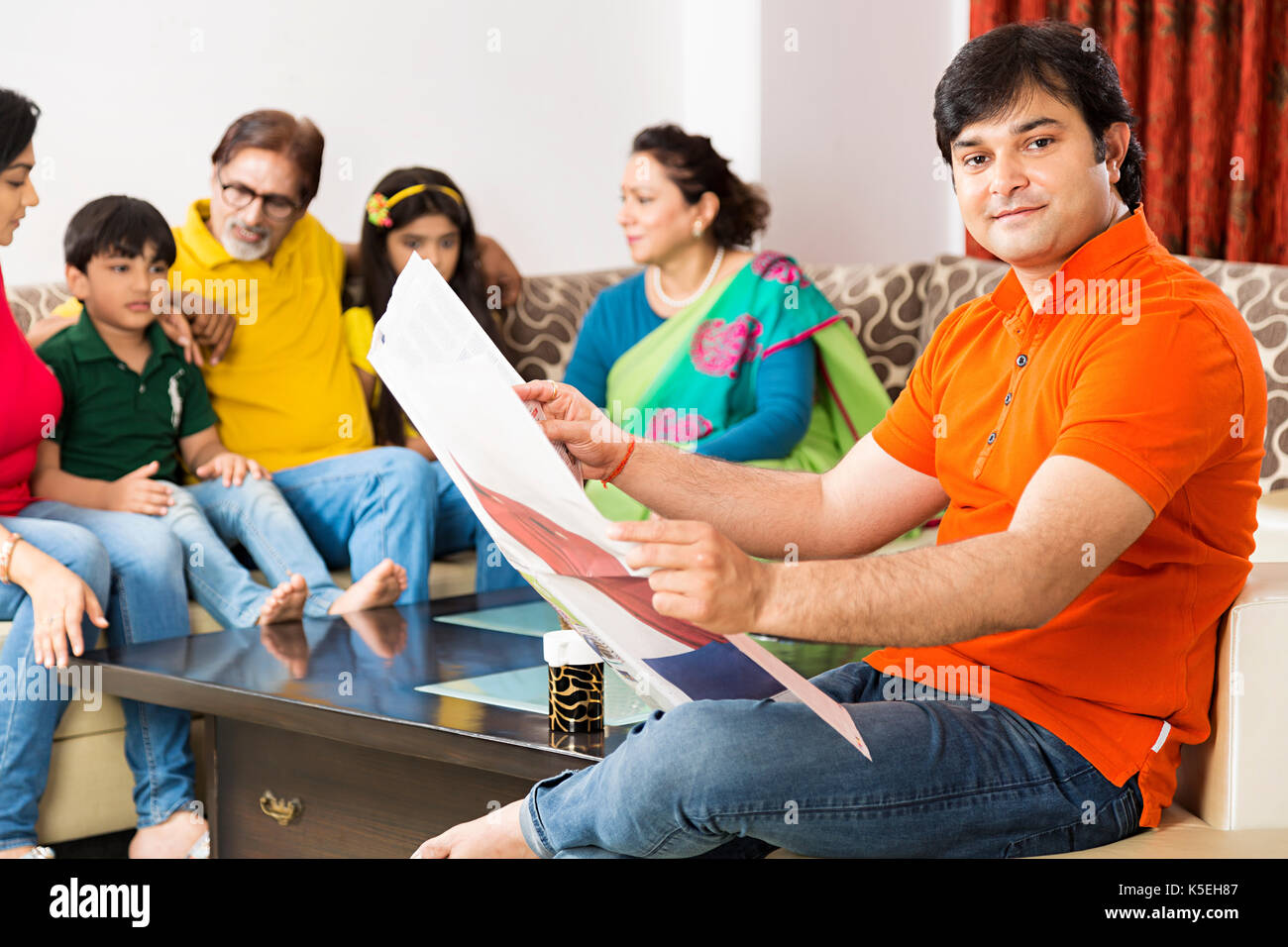 La famiglia felice divano con loro uomo leggendo il giornale in primo piano a home Foto Stock