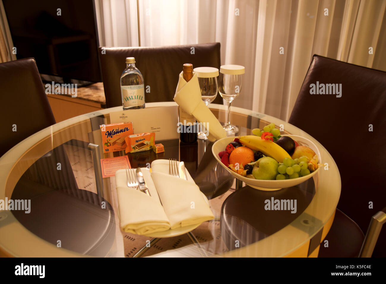 Vienna, Austria - aprile 28th, 2017: serata romantica con una bottiglia di vino rosso, dolci e frutta in camera di questo hotel di lusso su un tavolo con 3 sedie in pelle, Hilton suite penthouse Foto Stock