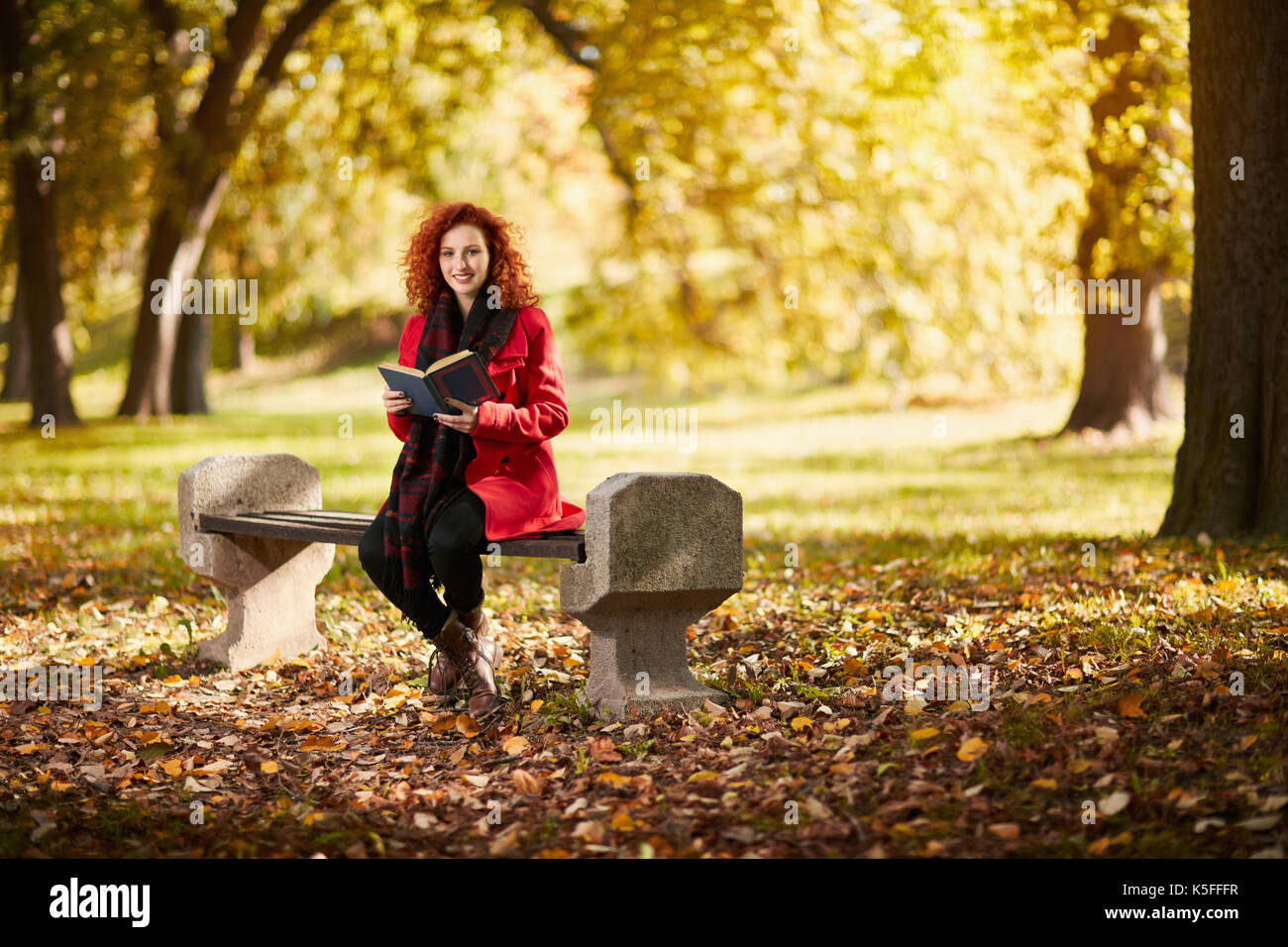 Curly redhead giovane femmina libro di lettura nel parco in autunno Foto Stock