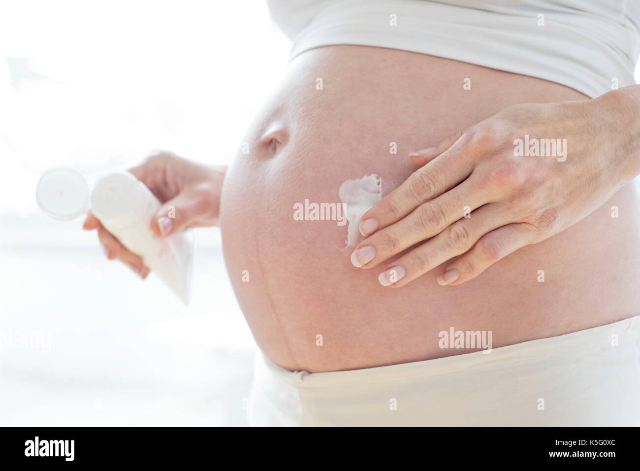 Donna incinta l'applicazione di crema idratante per il suo pancino. Foto Stock