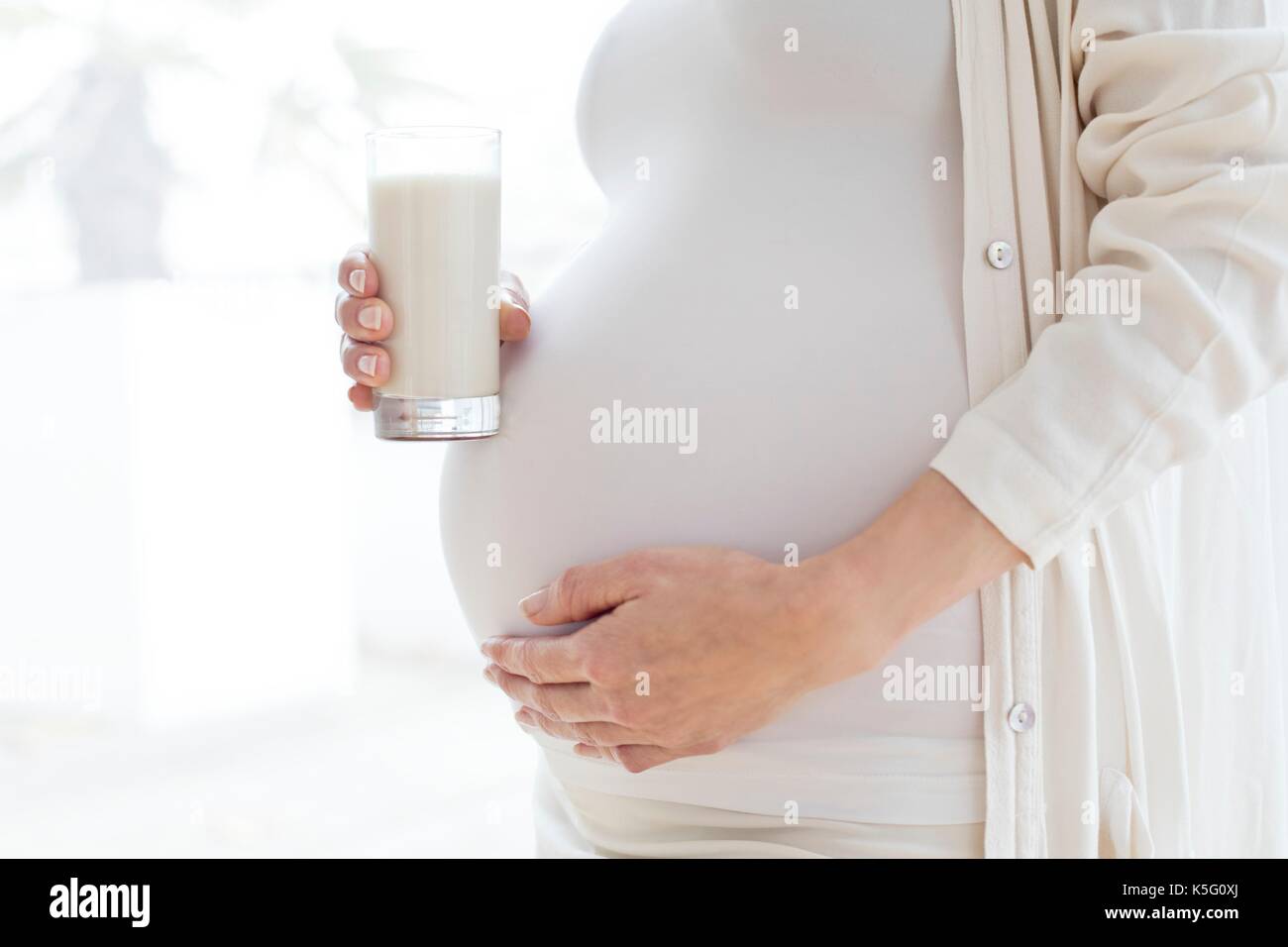 Donna incinta toccando la pancia tenendo un bicchiere di latte. Foto Stock