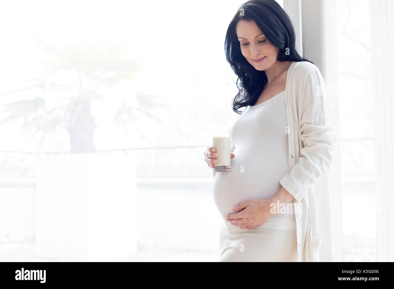 Donna incinta toccando la pancia tenendo un bicchiere di latte. Foto Stock