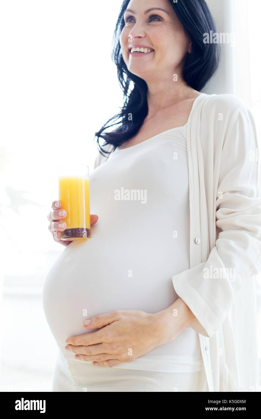 Donna incinta toccando la pancia tenendo un bicchiere di succo di frutta. Foto Stock