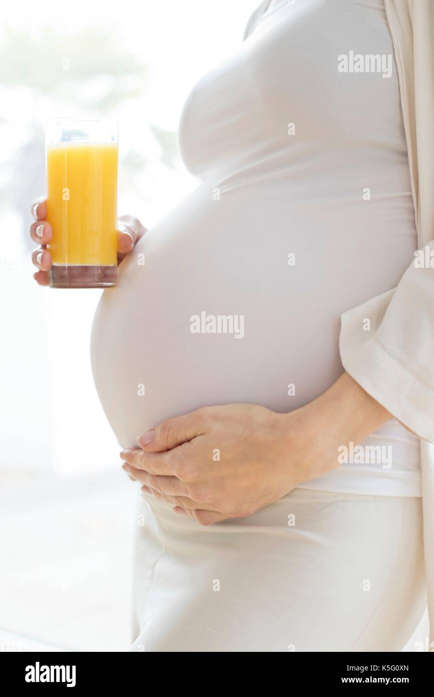 Donna incinta toccando la pancia tenendo un bicchiere di succo di frutta. Foto Stock