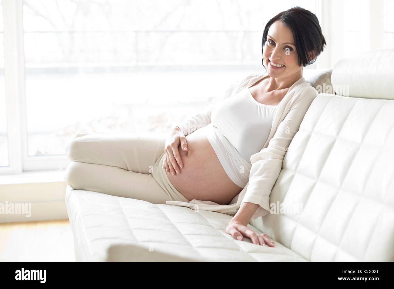 Donna incinta seduta sul divano di toccare la pancia. Foto Stock