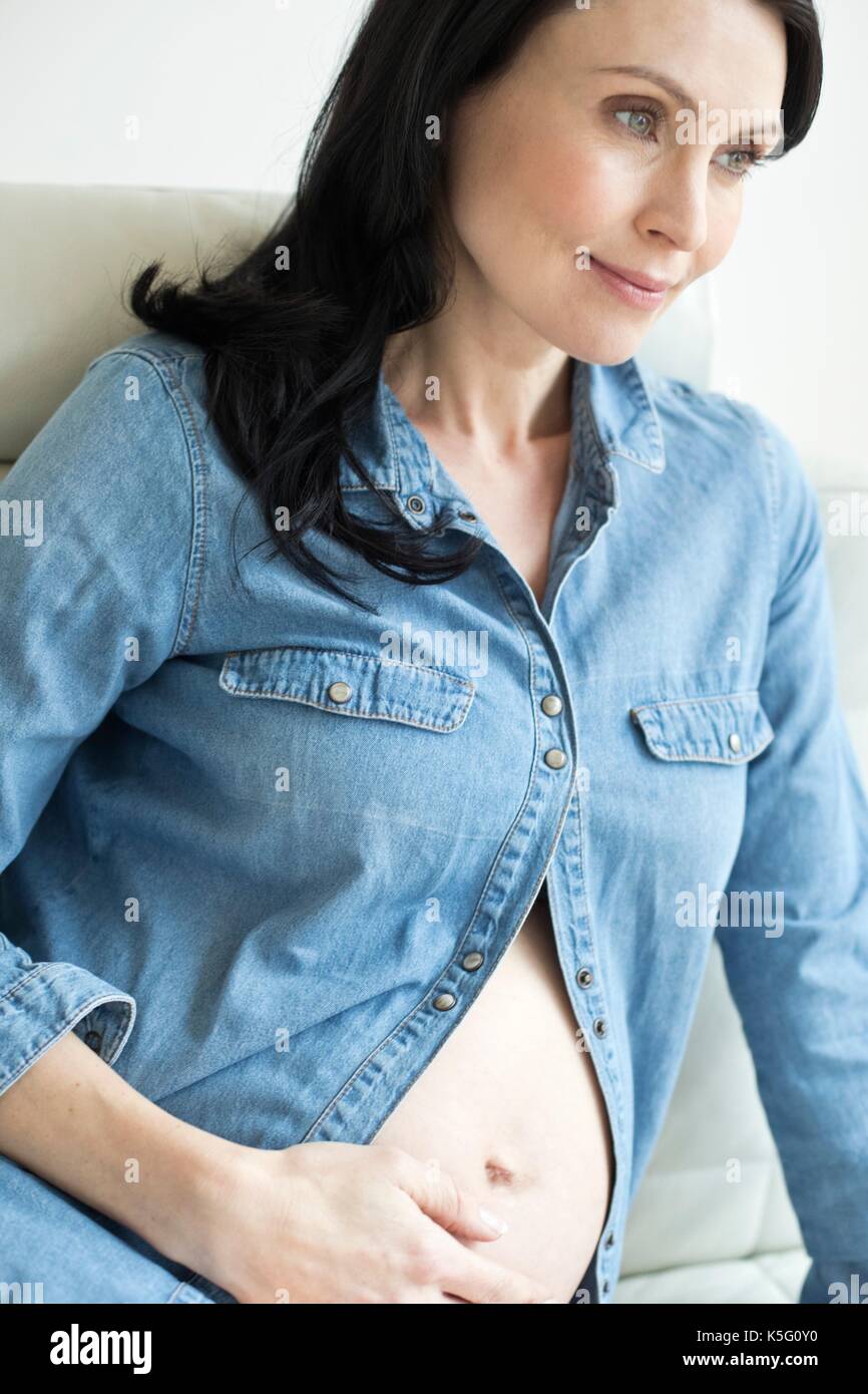 Donna incinta indossando shirt toccando la pancia. Foto Stock