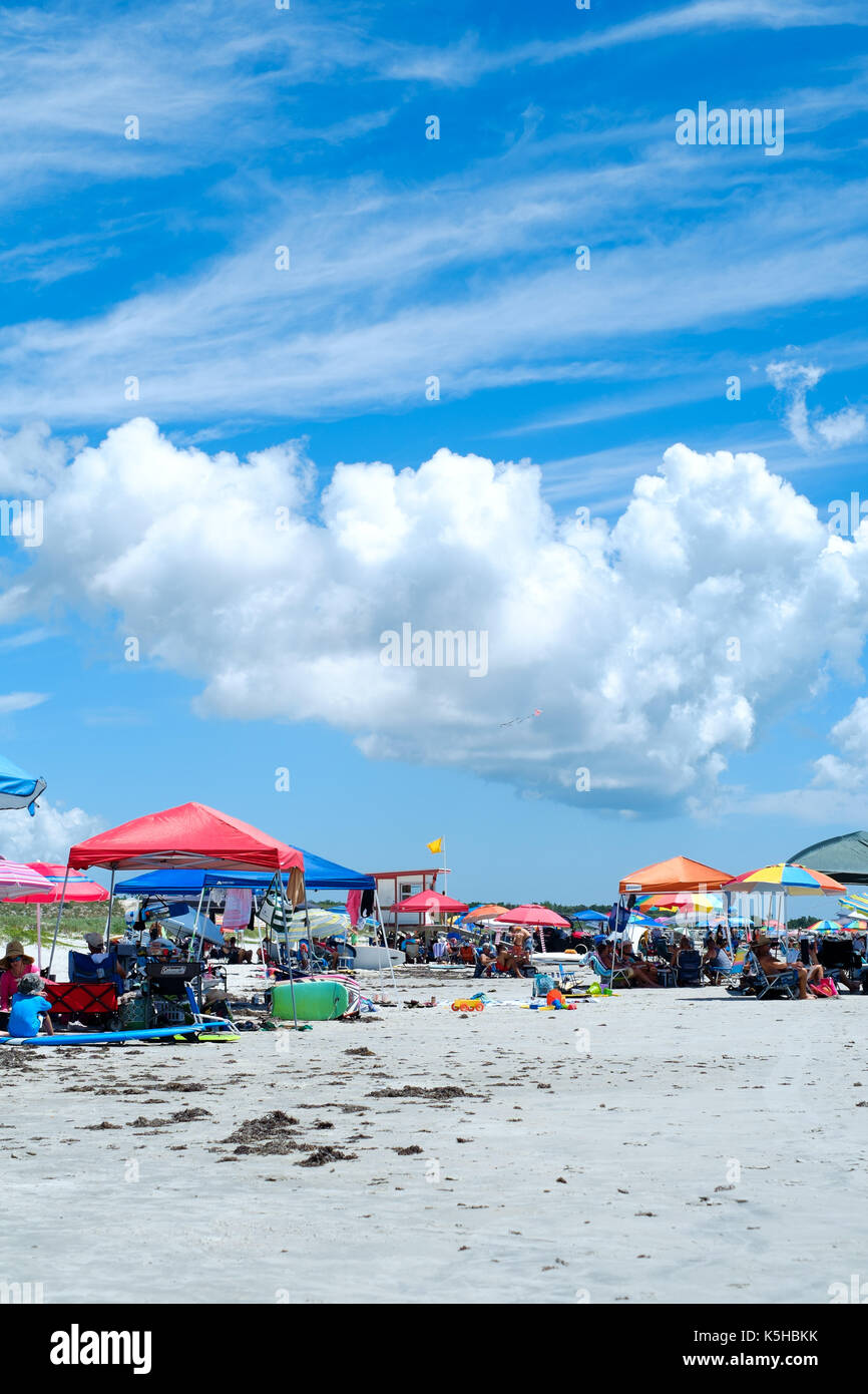 Frequentatori di spiaggia sotto il colorato canopys sun sulla spiaggia con sfondo di nuvoloso cielo blu Foto Stock