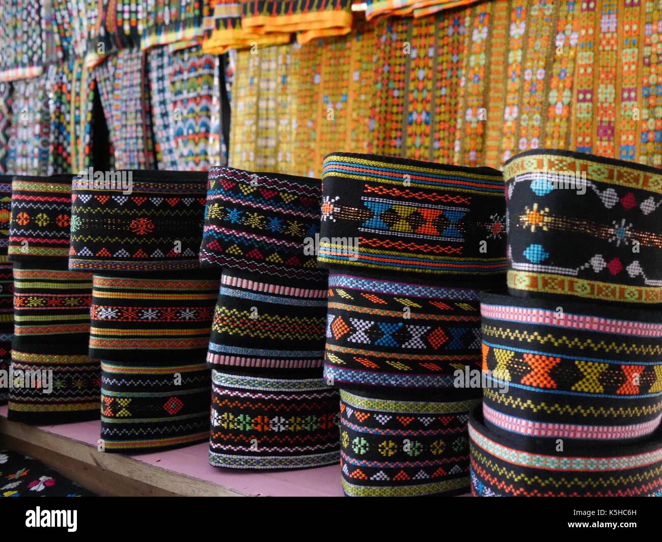 Close up di righe del modellato tradizionali cappelli indossati dagli uomini di sull isola di Flores, Indonesia con panni ikat mostrando dietro di loro Foto Stock