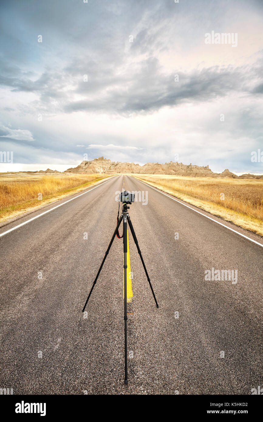 Foto professionali fotocamera su treppiede su una strada vuota al tramonto, la messa a fuoco della telecamera, di viaggio o di lavoro concetto, Parco nazionale Badlands, Dakota del Sud, Stati Uniti d'America Foto Stock