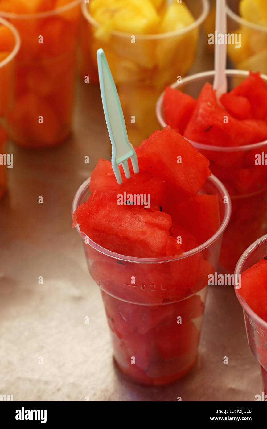Cucina di strada, selezione di insalate di frutta, fette tagliate fresche e mature e di cocomero melone cubetti in bicchieri di plastica con forche al mercato retail display di stallo, Foto Stock