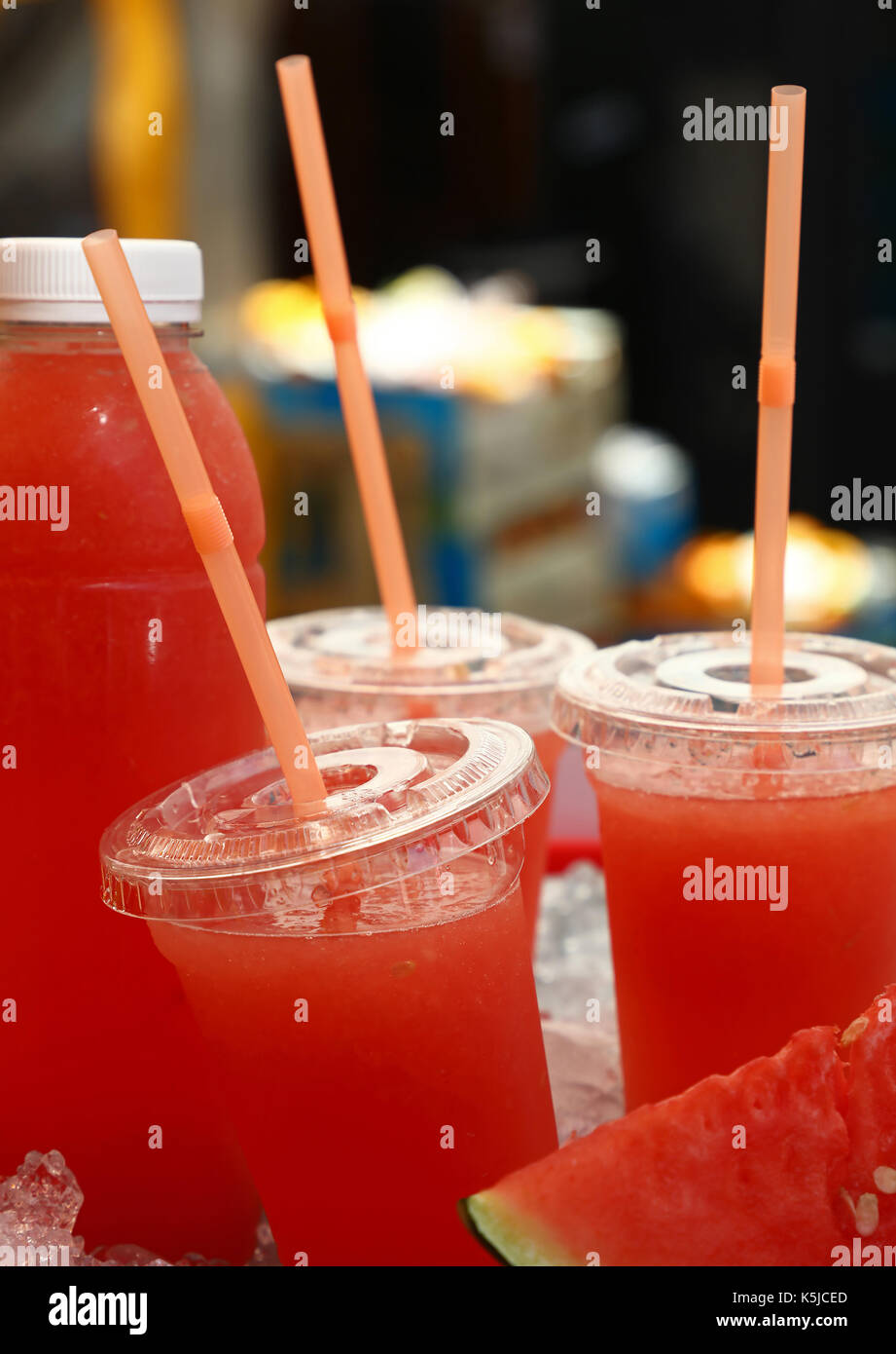 Spremuta fresca di red mature succo di anguria in bicchieri di plastica con cannucce e bottiglia sul ghiaccio nel mercato retail display di stallo, chiudere fino a basso angolo di visione Foto Stock