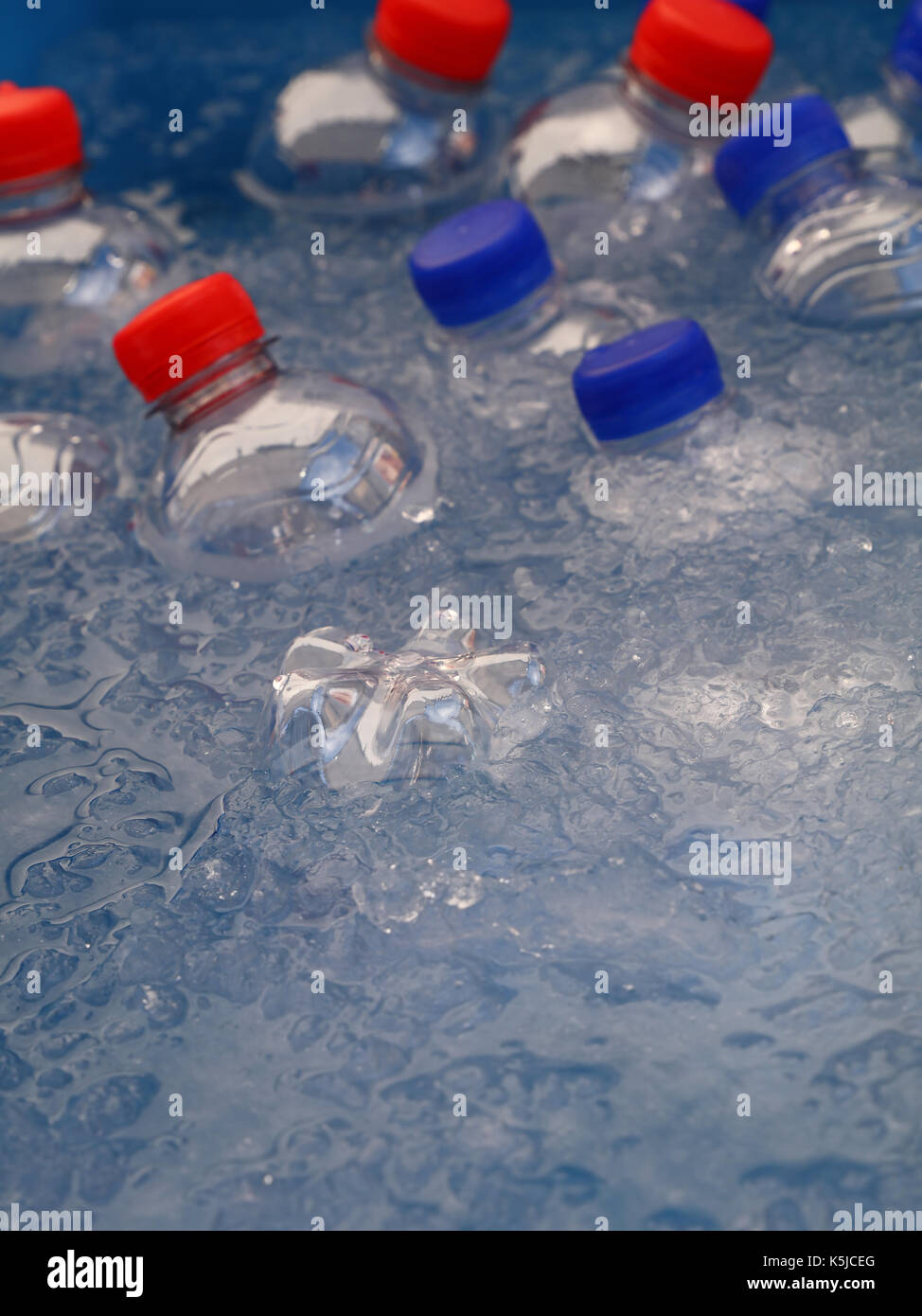 Bottiglie in plastica pet di freddo ancora e scintillante di bere acqua minerale con blu e cappucci rossi galleggiante e raffreddare in acqua e ghiaccio sul mercato al dettaglio di Foto Stock