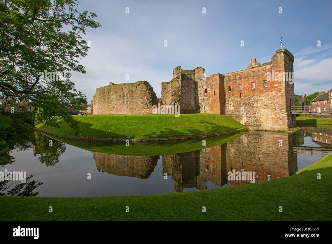 Splendida vista del XIII secolo il castello di rothesay con alte mura di pietra si riflette in superficie a specchio di acqua nel fossato sotto il cielo blu, isle of bute Scozia Scotland Foto Stock
