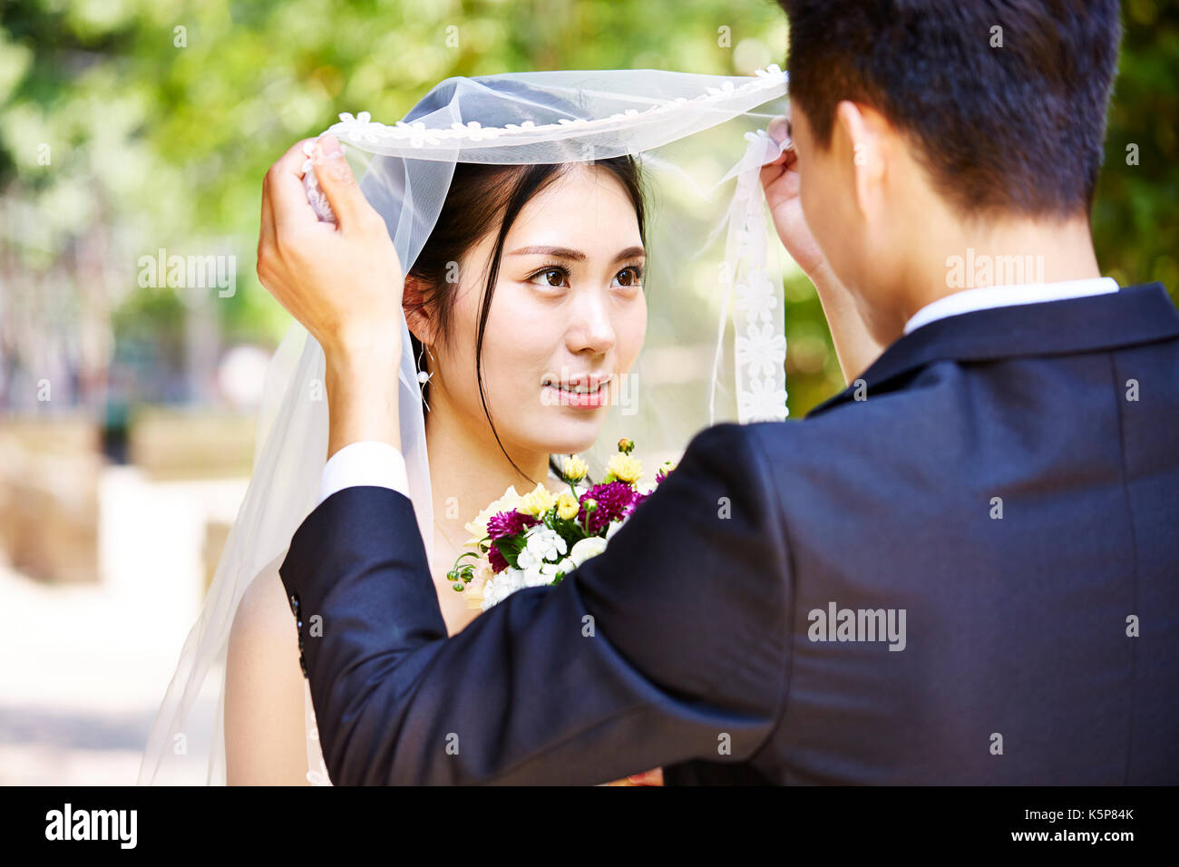 Asian groom sollevamento velo nuziale di kiss bella sposa. Foto Stock