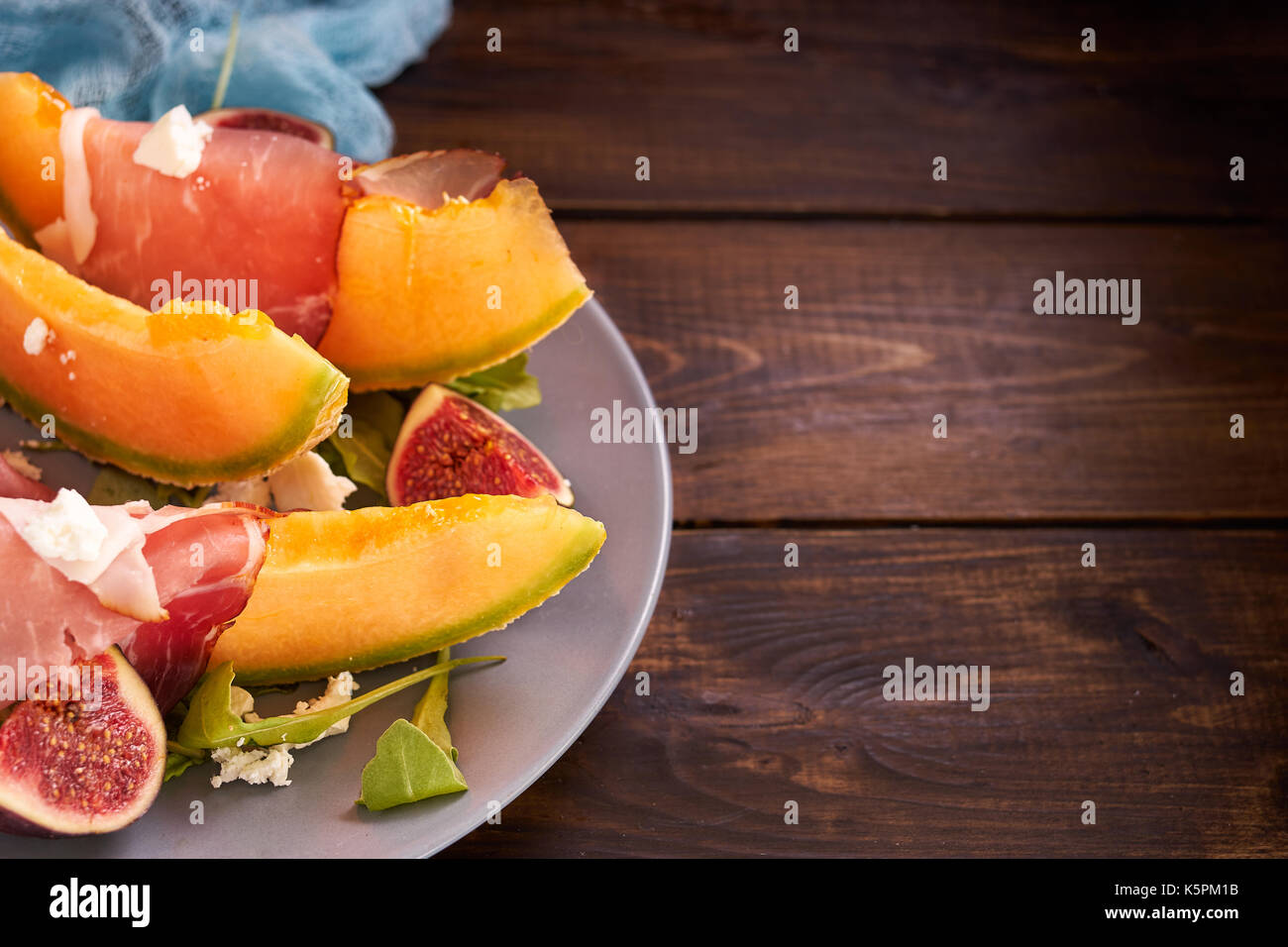 Mature melone dolce con prosciutto e rucola su sfondo rustico Foto Stock