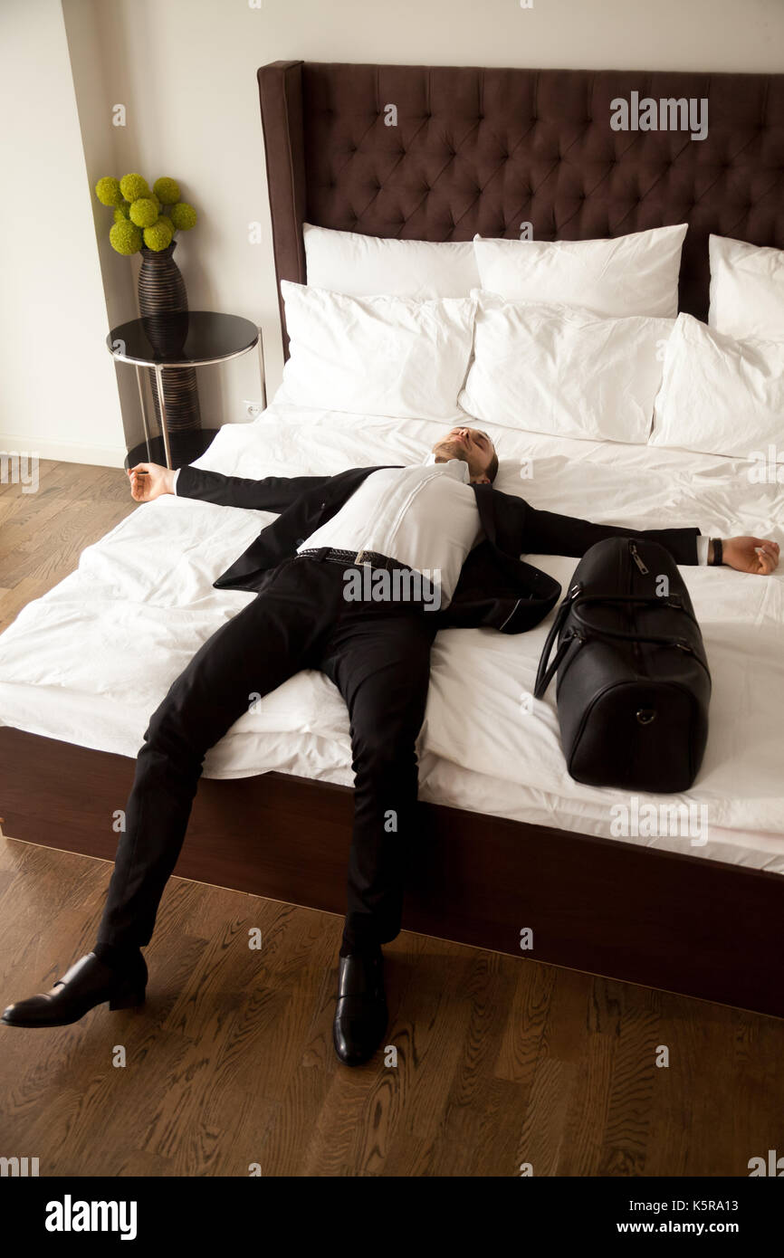 Esaurito imprenditore posa sul letto in camera d'albergo. Foto Stock