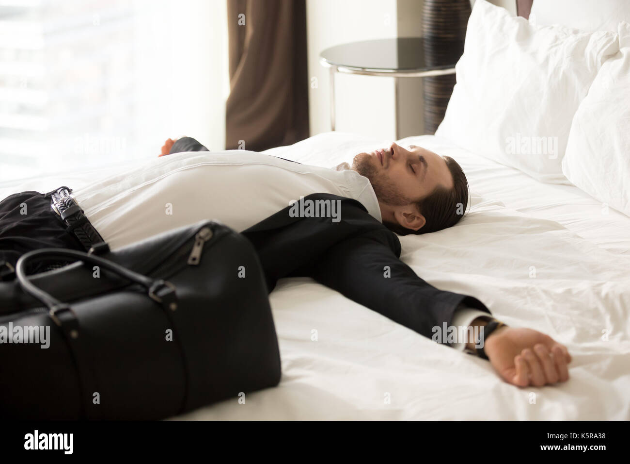 Esaurito imprenditore posa sul letto in camera d'albergo. Foto Stock