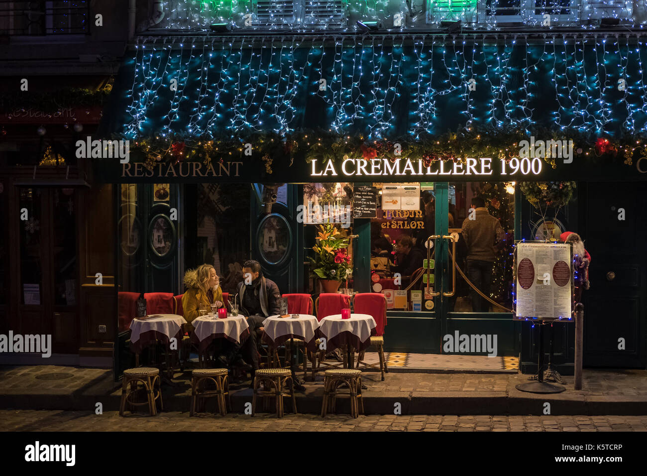 Un giovane su una romantica terrazza di un ristorante sulla Place du Tertre a Montmartre a Parigi sulla sera di Natale con luci colorate. Foto Stock