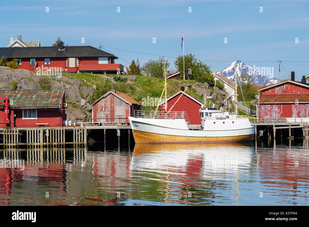 La pesca in barca ormeggiata in porto con Rorbu capanne su palafitte in villaggio norvegese. Ballstad, Vestvågøya, Isole Lofoten, Nordland, Norvegia Foto Stock