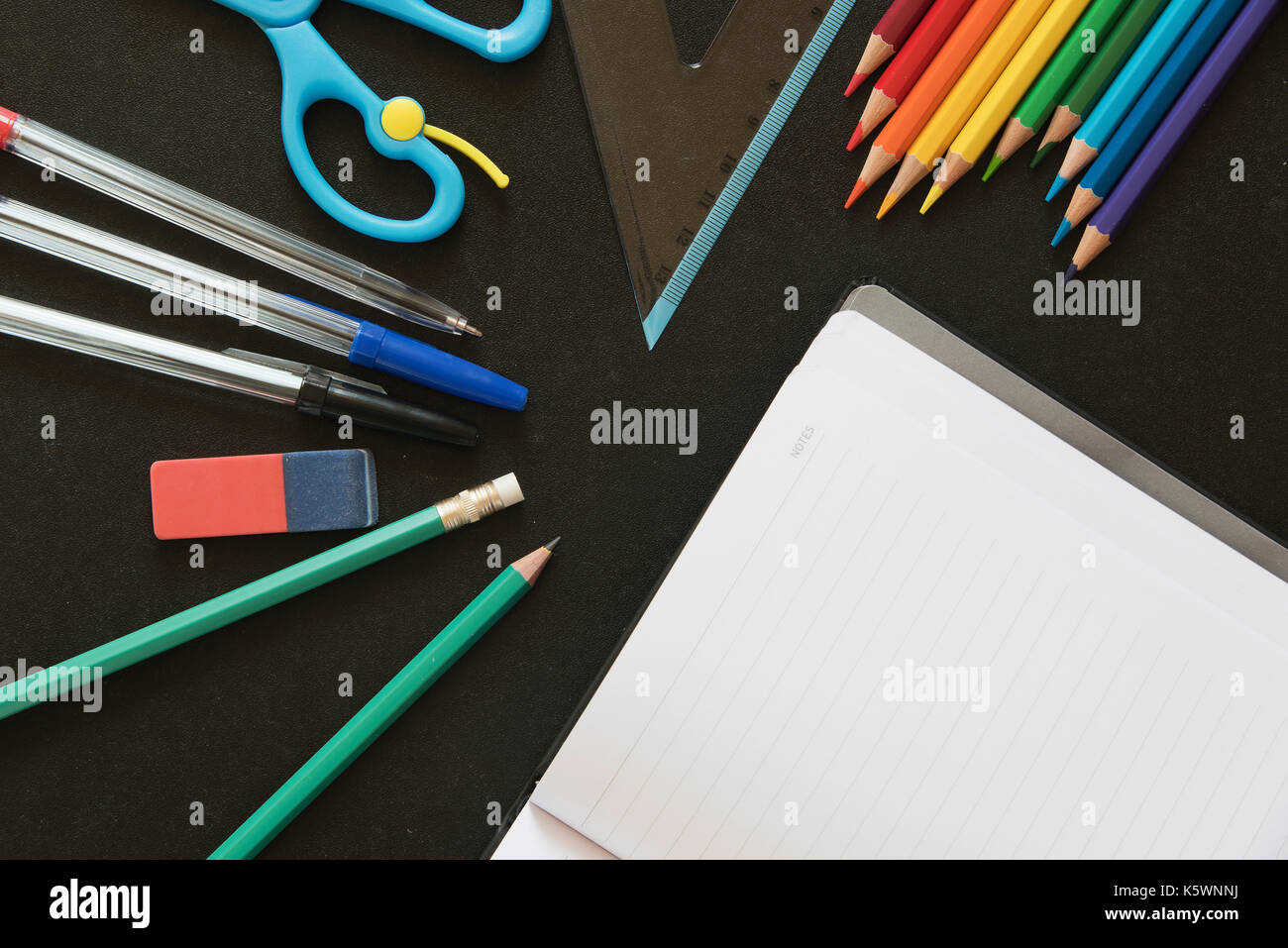 Diversi tipi di scuola e ufficio utensili al buio su un superficie di lavagna con un notebook vuoto Foto Stock