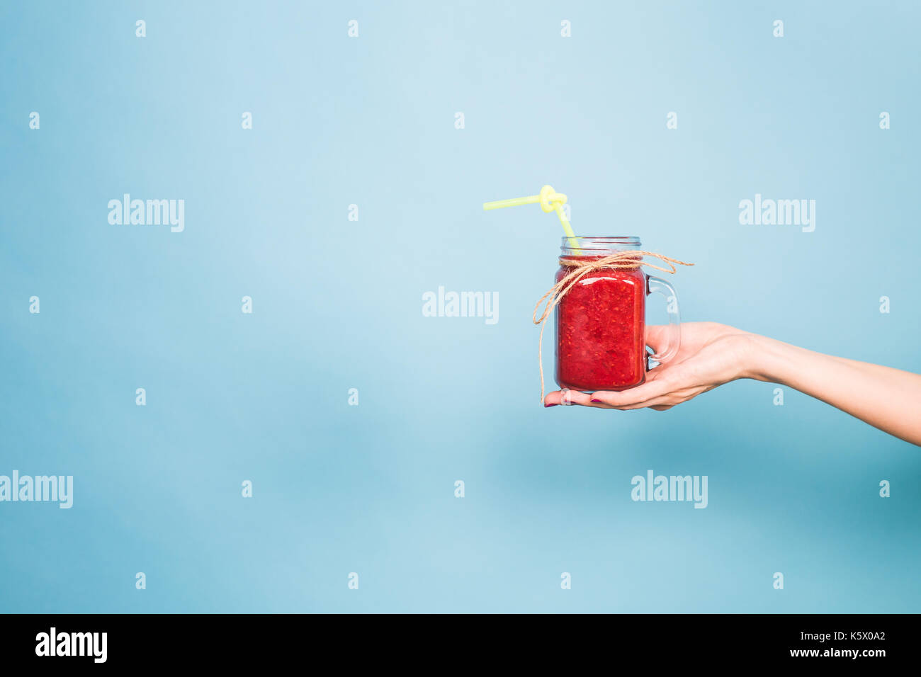 Donna di mano che trattiene il vetro di fragola e frullato rasberry su sfondo blu. Foto Stock