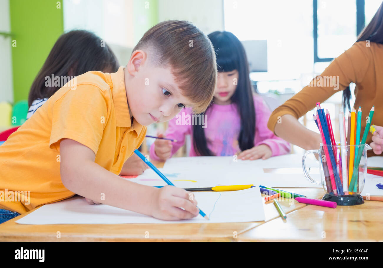 I bambini di età prescolare Disegno con matite colorate su carta bianca sulla tavola in aula con gli amici e il maestro,Kindergarten concetto di istruzione Foto Stock