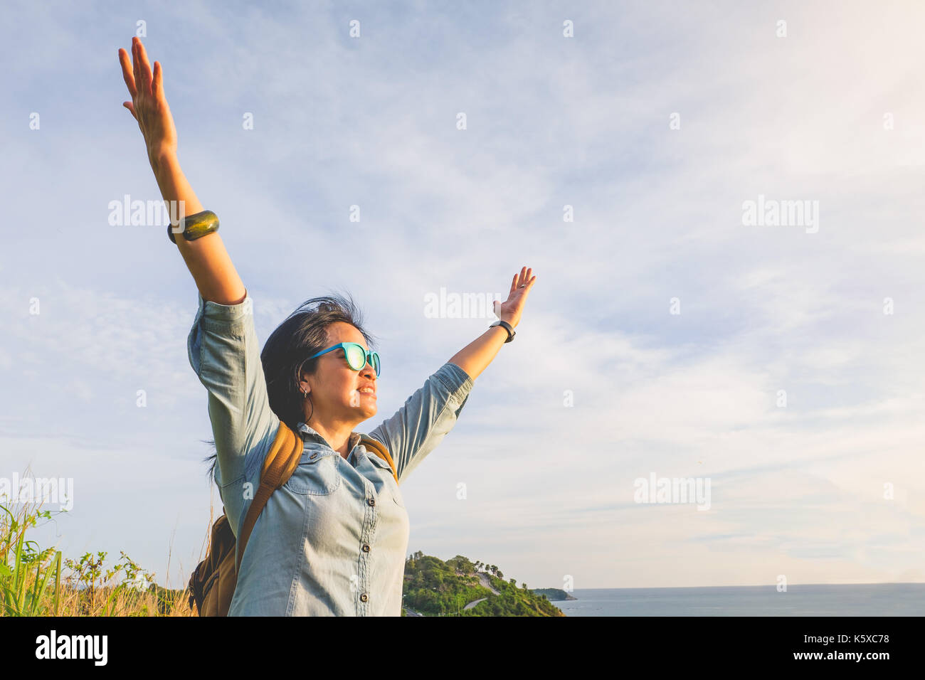 Felice giovane donna di viaggiatori ha sollevato il braccio fino a cielo gustando una bella della natura alla cima della montagna e vista mare,libertà wanderlust backpacker concetto,v Foto Stock