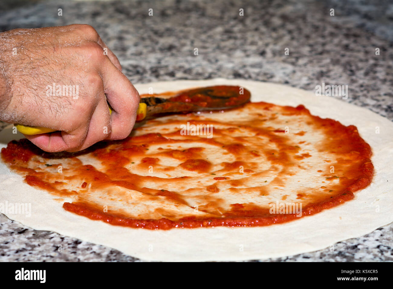 Preparate la pasta per pizza con salsa di pomodoro. messa a fuoco selettiva.close-up di man mano in azione Foto Stock
