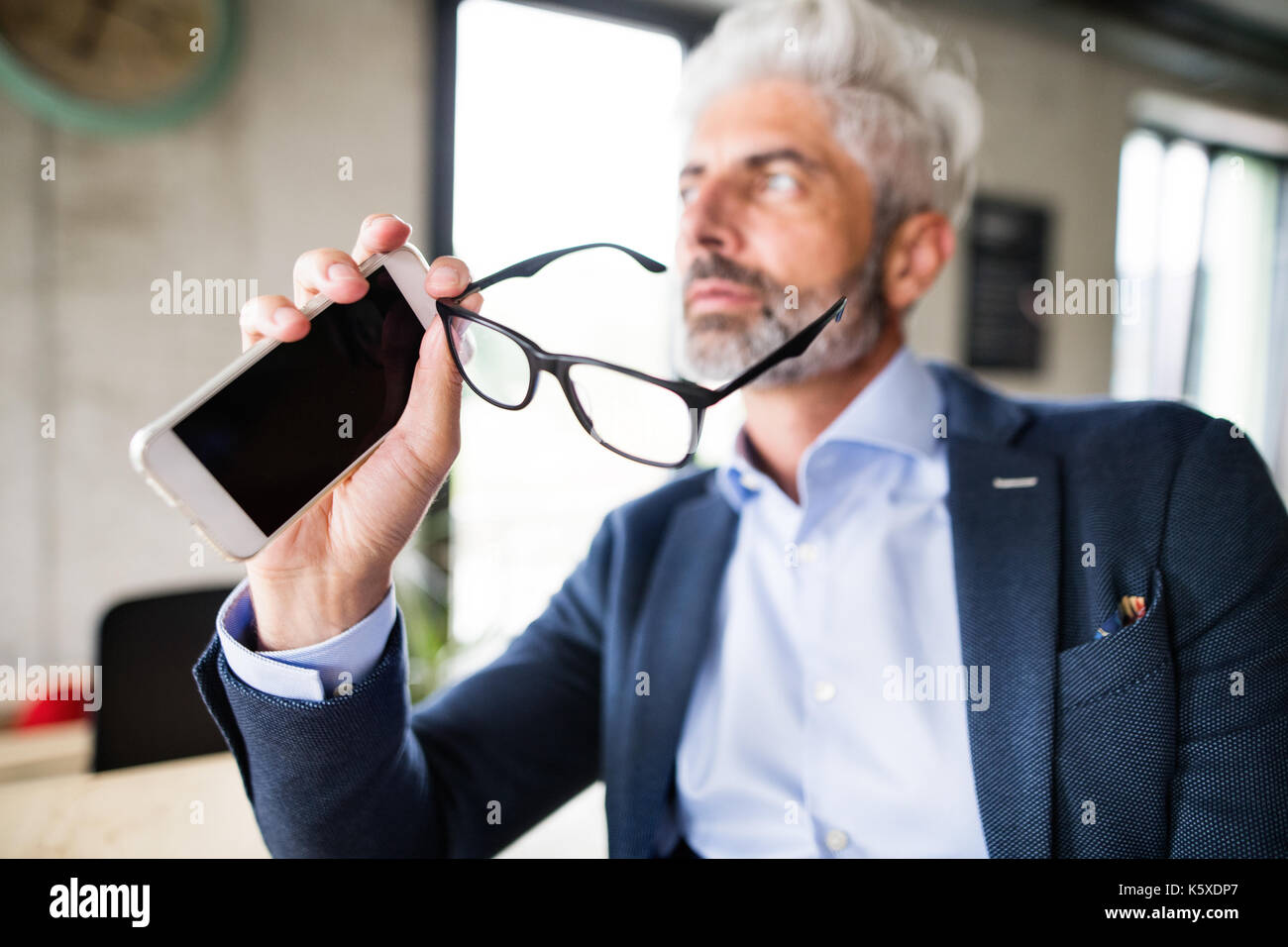 Imprenditore maturo con lo smartphone in ufficio. Foto Stock