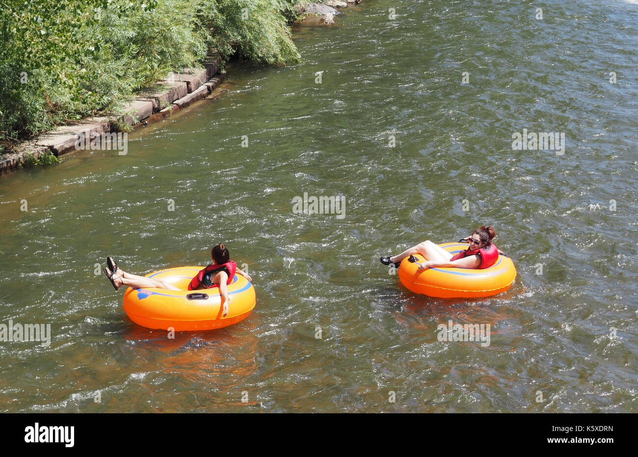 Golden, co - 12 agosto: due femmine non identificato approfittare di una bella giornata estiva e galleggiare su tubi in chiaro fiume che corre attraverso la matassa Foto Stock