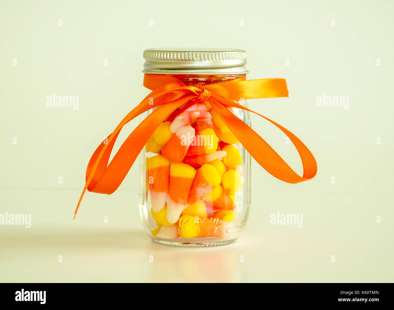Mason vaso riempito con la caramella di mais e legate con nastro arancione isolata su uno sfondo a tinta unita Foto Stock