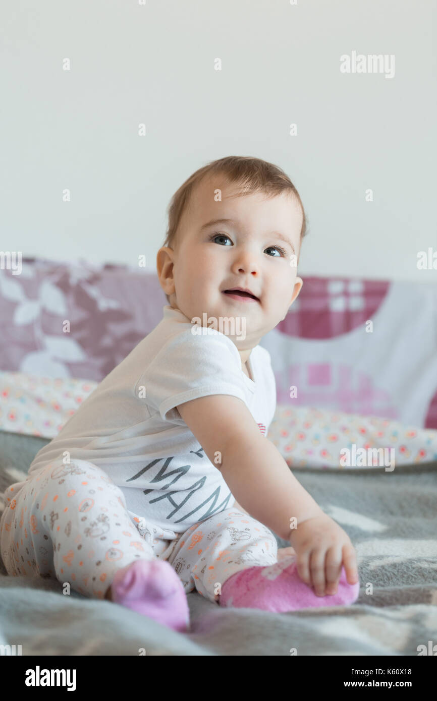 Colpo verticale. piccolo bimbo sorridente si siede sul letto di casa. Foto Stock