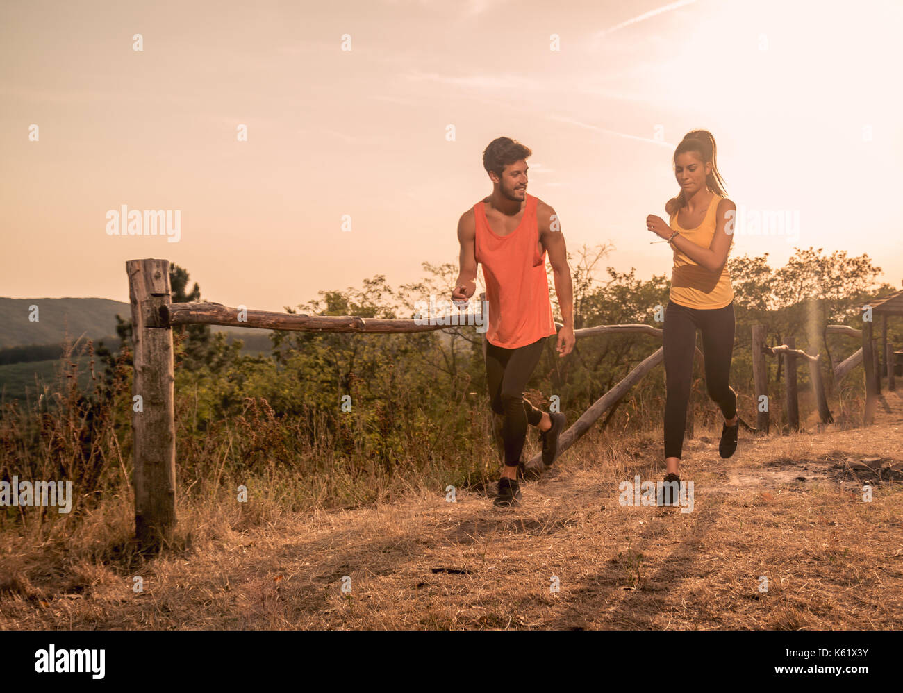 Due giovani, uomo donna, correndo all'aperto, natura caldo giorno d'estate e caldi colori, indumenti sportivi Foto Stock