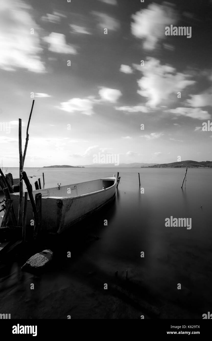 Una piccola barca da pesca su un lago, con perfettamente ancora acqua e nuvole in movimento Foto Stock