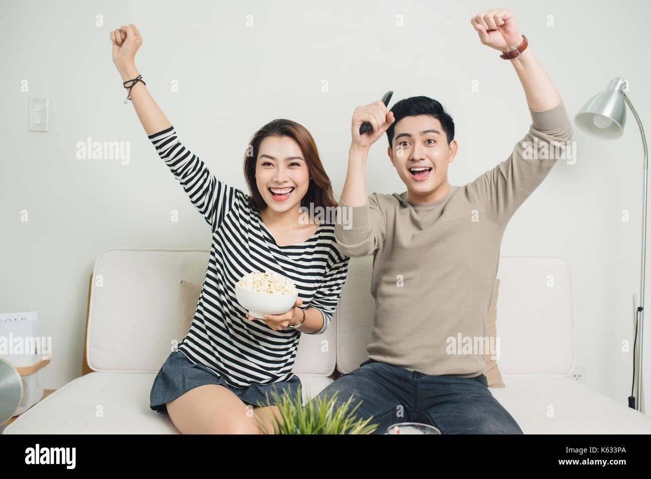 Eccitato giovane coppia asiatica di guardare la tv e mangiare popcorn Foto Stock