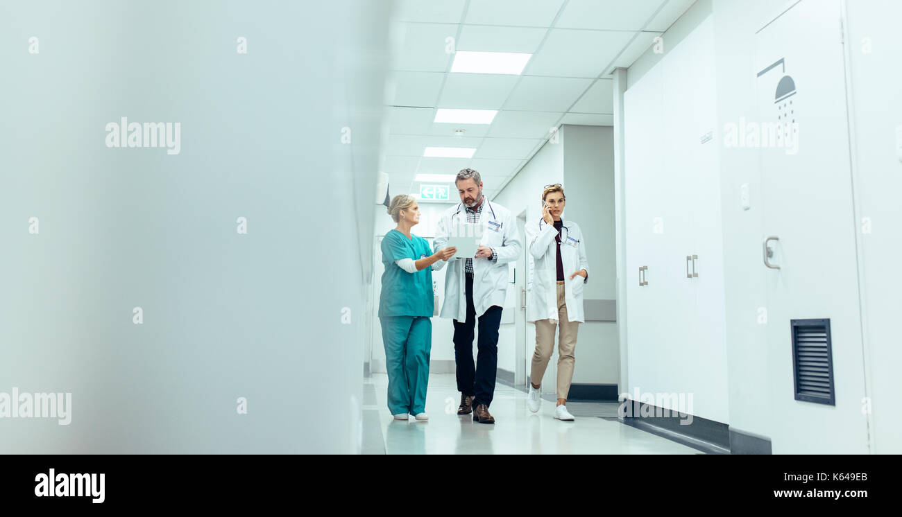 Il gruppo di medici con appunti a camminare lungo il corridoio dell'ospedale. Medico e infermiere a discutere di referto medico con il collega femmina parlando sul mobile pho Foto Stock